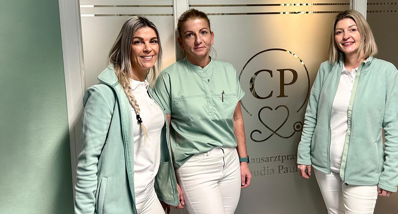 Claudia Paulick mit Schwester Steffi und Schwester Anne vor einer Glaswand mit Logo